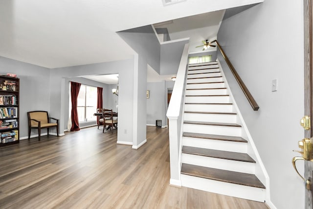 stairway with ceiling fan with notable chandelier, baseboards, wood finished floors, and visible vents