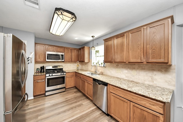 kitchen with tasteful backsplash, a sink, light wood finished floors, appliances with stainless steel finishes, and visible vents