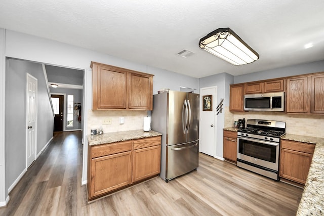 kitchen featuring light wood finished floors, stainless steel appliances, visible vents, and decorative backsplash