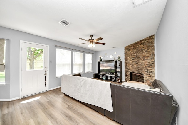 living area with light wood-style flooring, a stone fireplace, a wealth of natural light, and ceiling fan