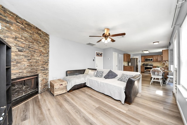 living room featuring a fireplace, light wood-style floors, visible vents, and a ceiling fan