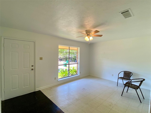 interior space with a textured ceiling, visible vents, a ceiling fan, and baseboards