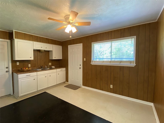 kitchen with white cabinets, a textured ceiling, a ceiling fan, wood walls, and light floors
