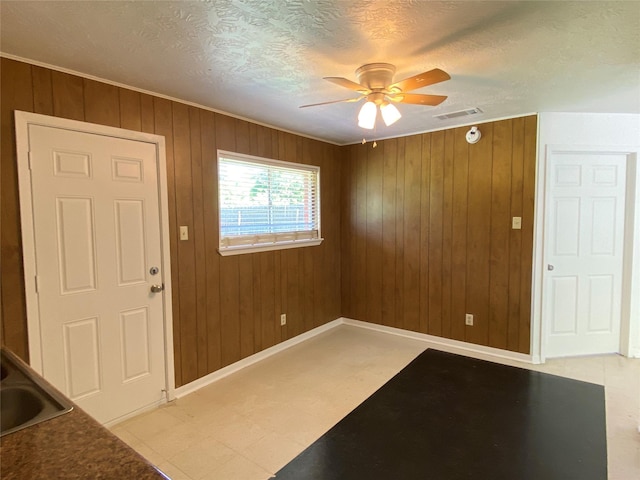 entryway featuring a textured ceiling, visible vents, a ceiling fan, wood walls, and light floors