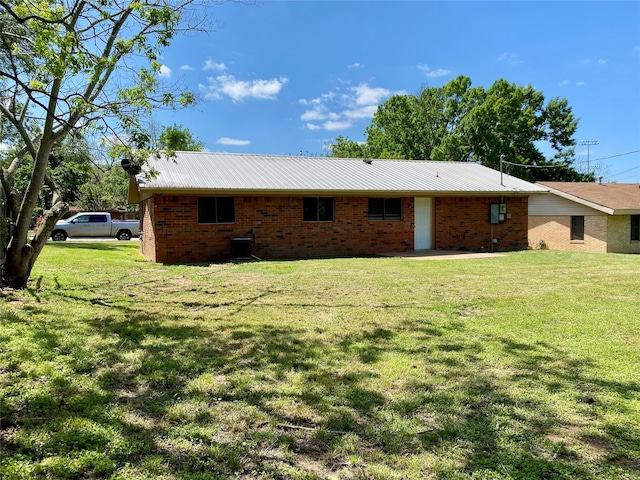 back of house with brick siding, a yard, central air condition unit, and metal roof