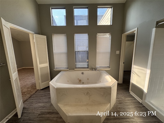 full bathroom featuring a high ceiling, baseboards, wood finished floors, and a jetted tub