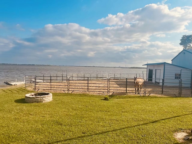 view of grassy yard featuring a fire pit, a water view, and an outdoor structure
