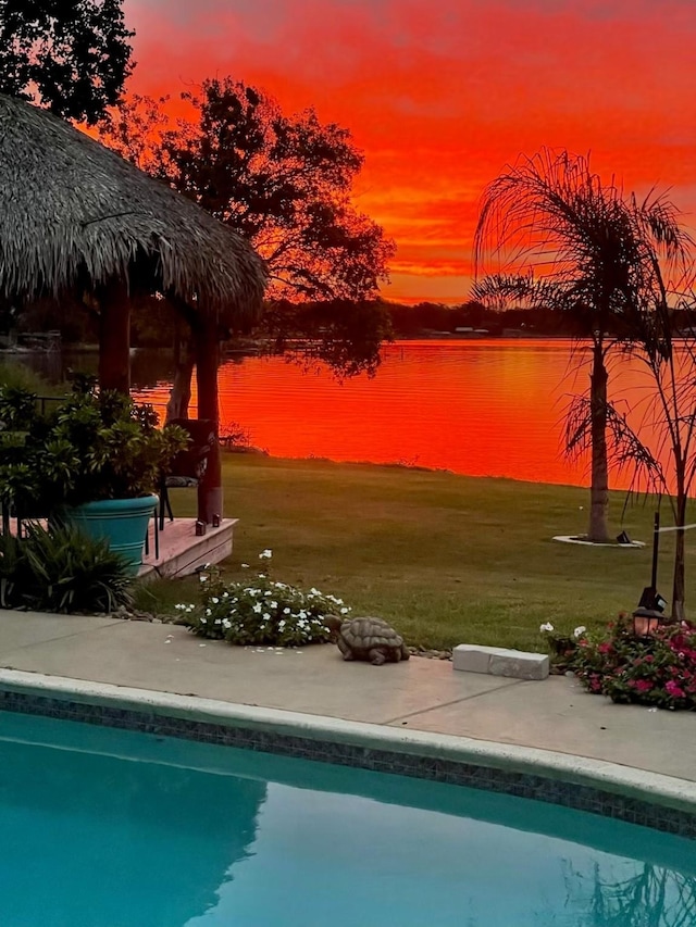 pool at dusk featuring a water view, an outdoor pool, and a yard