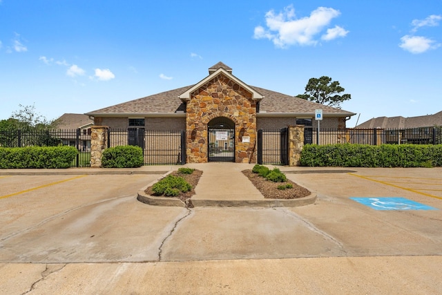 view of front of house with stone siding, uncovered parking, a gate, and a fenced front yard