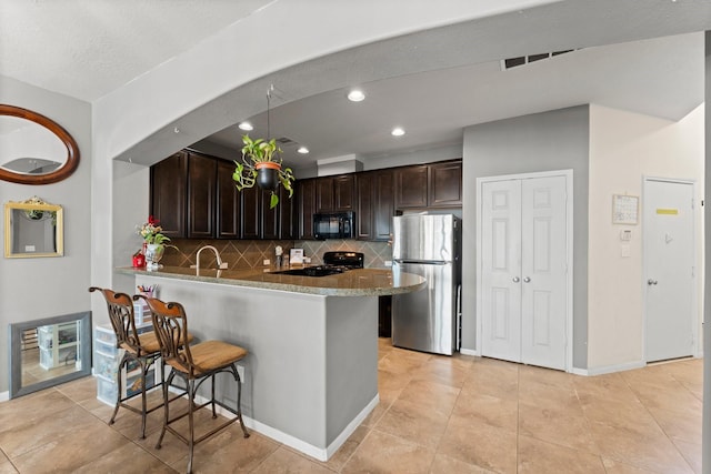 kitchen with a kitchen breakfast bar, light stone counters, dark brown cabinets, decorative backsplash, and black appliances