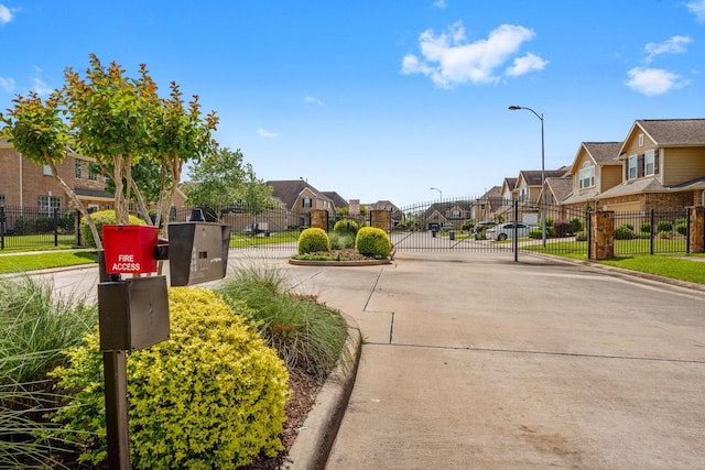 view of road with curbs, a gate, a residential view, street lights, and a gated entry