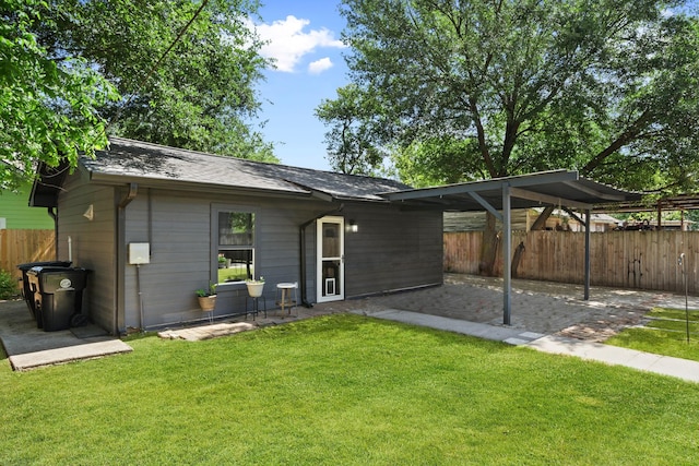 rear view of house with fence, a shingled roof, a patio, a carport, and a lawn