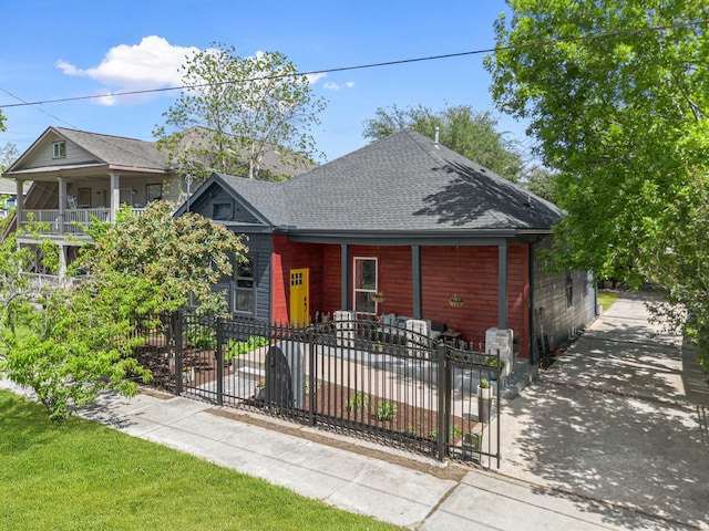 view of front of home featuring a porch, roof with shingles, and a fenced front yard