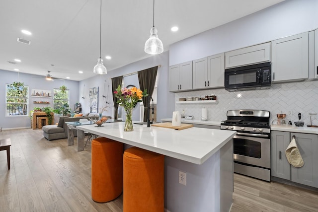 kitchen featuring stainless steel gas stove, black microwave, light countertops, gray cabinetry, and visible vents