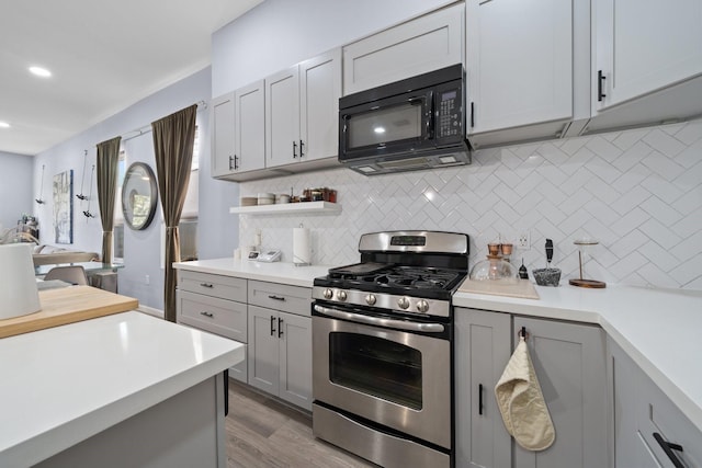 kitchen with black microwave, light countertops, gas range, and tasteful backsplash