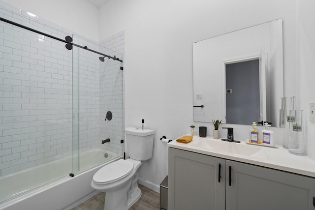 bathroom featuring wood finished floors, toilet, vanity, baseboards, and bath / shower combo with glass door