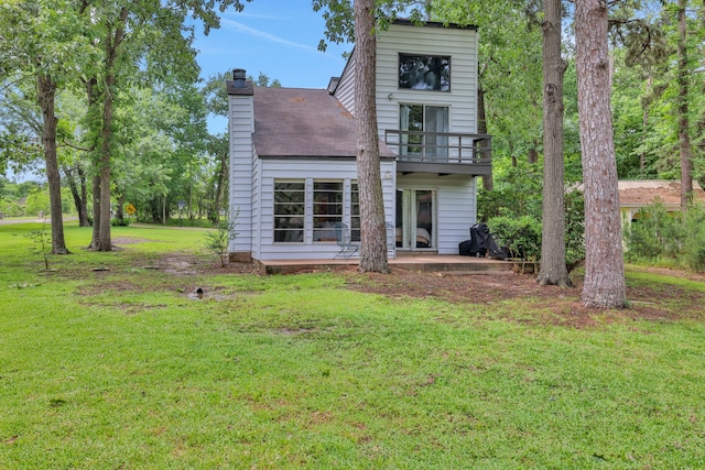 rear view of house featuring a balcony, a patio area, a yard, and a chimney