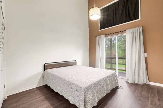bedroom with baseboards, a high ceiling, dark wood-style floors, and access to exterior