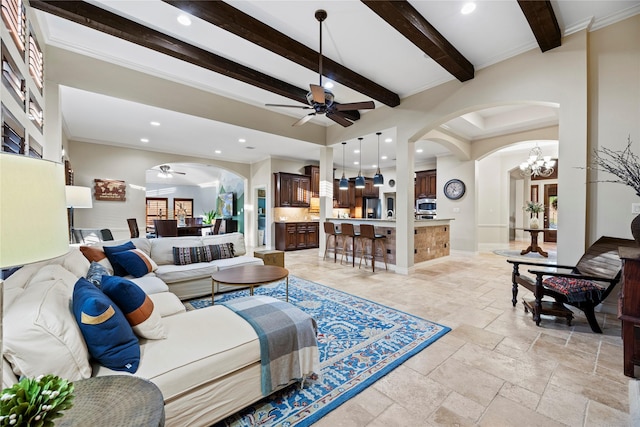 living room with ceiling fan with notable chandelier, stone tile floors, arched walkways, and beamed ceiling