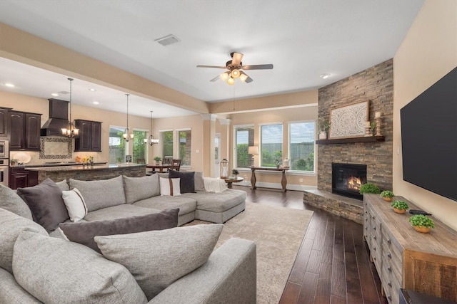 living room with dark wood-style flooring, visible vents, recessed lighting, ceiling fan with notable chandelier, and a stone fireplace
