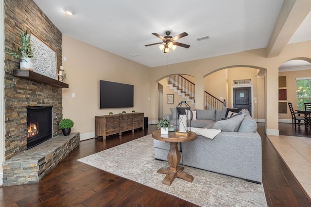 living area featuring arched walkways, stairway, ceiling fan, a fireplace, and wood-type flooring