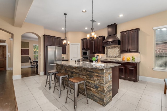kitchen featuring stainless steel appliances, arched walkways, decorative backsplash, stone countertops, and premium range hood