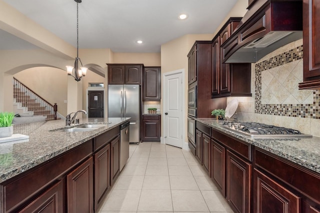 kitchen with stainless steel appliances, arched walkways, a sink, custom exhaust hood, and stone countertops