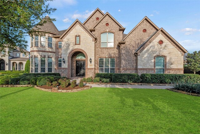 french country style house with brick siding and a front yard