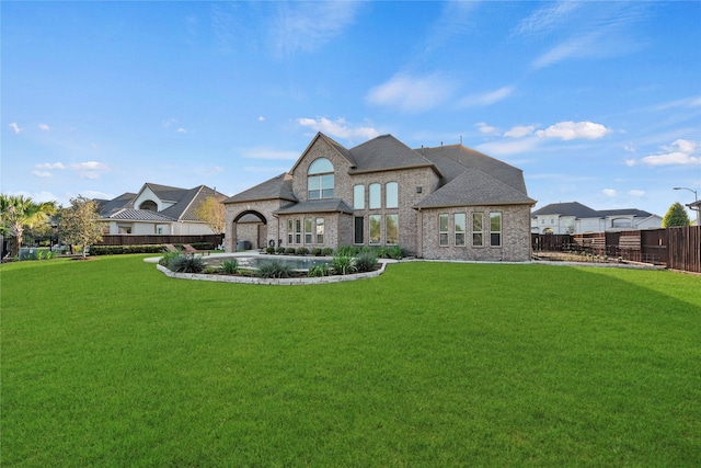 back of house with a lawn, fence, and brick siding