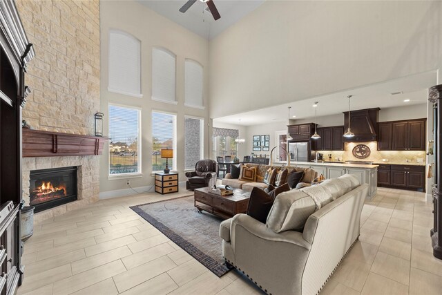 living area with a stone fireplace, a high ceiling, and ceiling fan