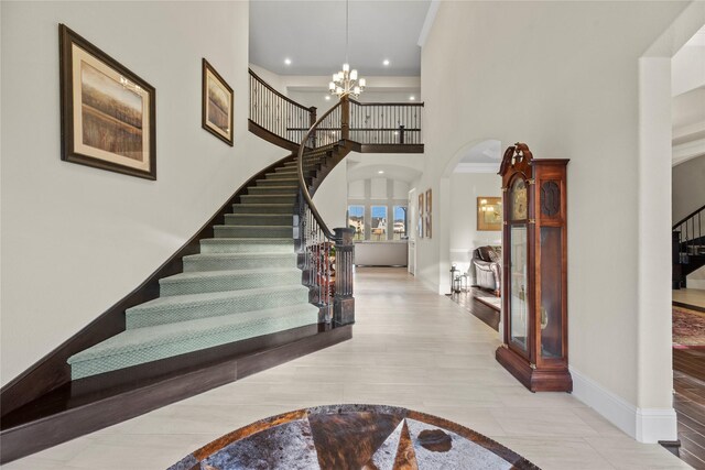 entryway with stairway, arched walkways, an inviting chandelier, a towering ceiling, and baseboards