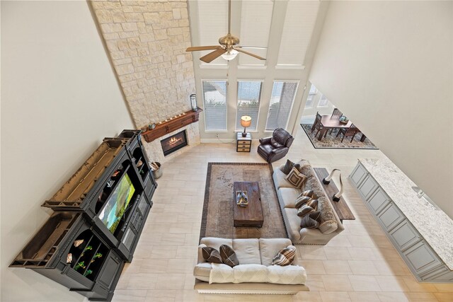 living room featuring ceiling fan, a high ceiling, and a stone fireplace
