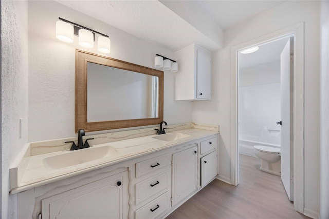 bathroom featuring double vanity, wood finished floors, toilet, and a sink