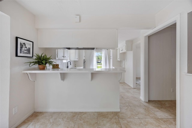 kitchen with light tile patterned flooring, a breakfast bar area, light countertops, white cabinets, and a peninsula