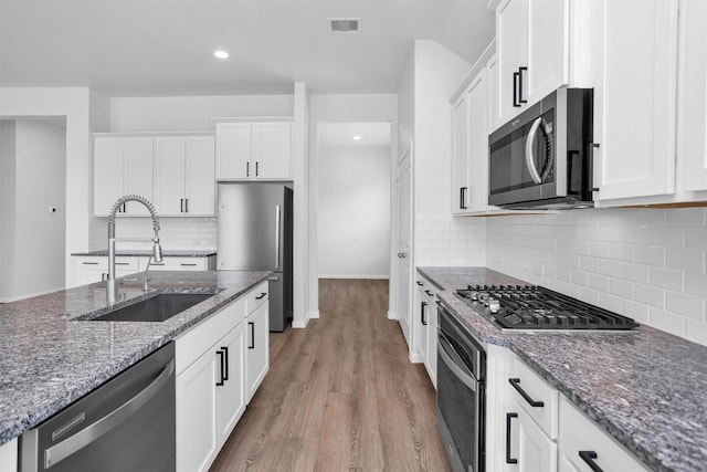 31411 Raleigh Creek Dr, Tomball, TX 77375 - kitchen featuring stainless steel appliances, a sink, light wood-style flooring, white cabinetry, and dark stone countertops