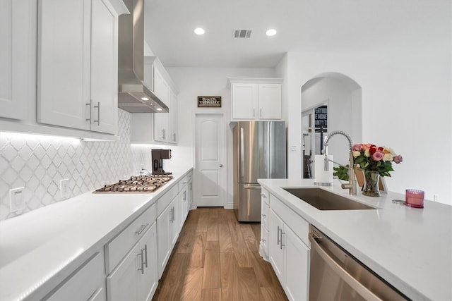 kitchen with a sink, stainless steel appliances, wall chimney exhaust hood, visible vents, and arched walkways