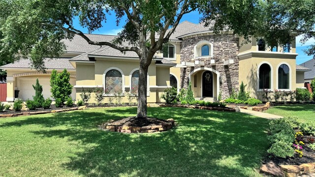 view of front facade with stone siding, a garage, a front yard, and stucco siding