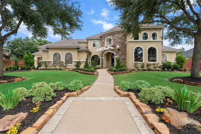 mediterranean / spanish home featuring stucco siding, stone siding, a front yard, and fence