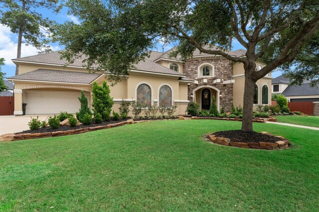 mediterranean / spanish house with a front lawn, stone siding, a garage, stucco siding, and driveway