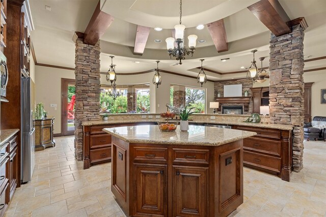 kitchen featuring a notable chandelier, stone tile floors, a large island, ornate columns, and ornamental molding