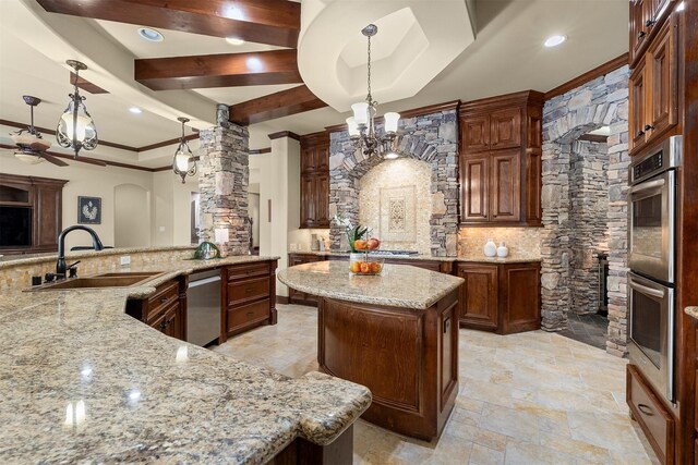 kitchen featuring light stone countertops, a sink, a center island, stainless steel appliances, and decorative columns