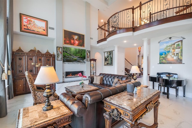 living room with stairway, a glass covered fireplace, marble finish floor, a towering ceiling, and ornate columns