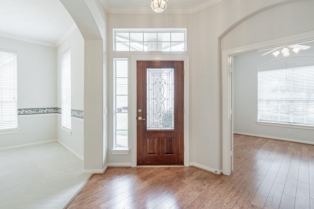 foyer entrance with hardwood / wood-style flooring, arched walkways, baseboards, and crown molding