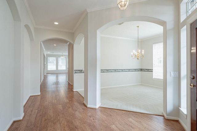 hall with a chandelier, arched walkways, wood-type flooring, baseboards, and ornamental molding