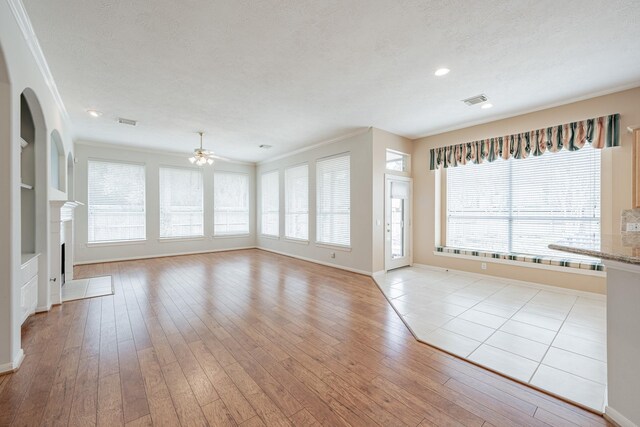 unfurnished living room featuring baseboards, crown molding, visible vents, and light wood-style flooring