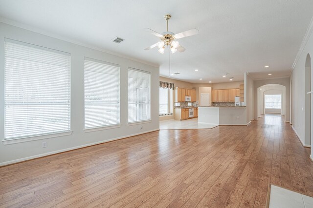 unfurnished living room with ceiling fan, arched walkways, light wood finished floors, ornamental molding, and visible vents