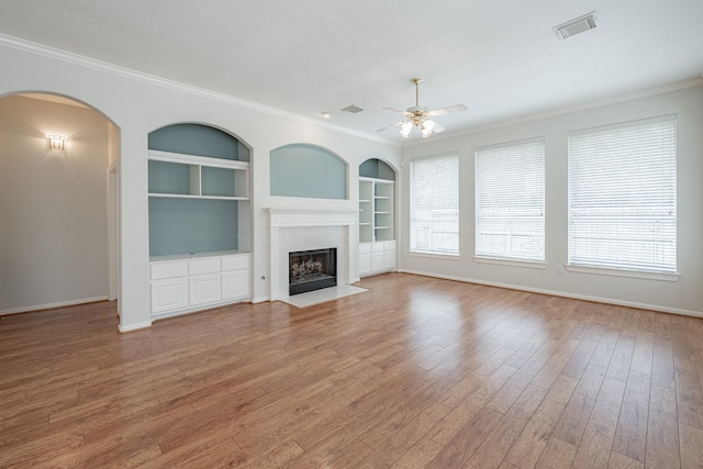 unfurnished living room with a ceiling fan, wood finished floors, built in shelves, baseboards, and visible vents