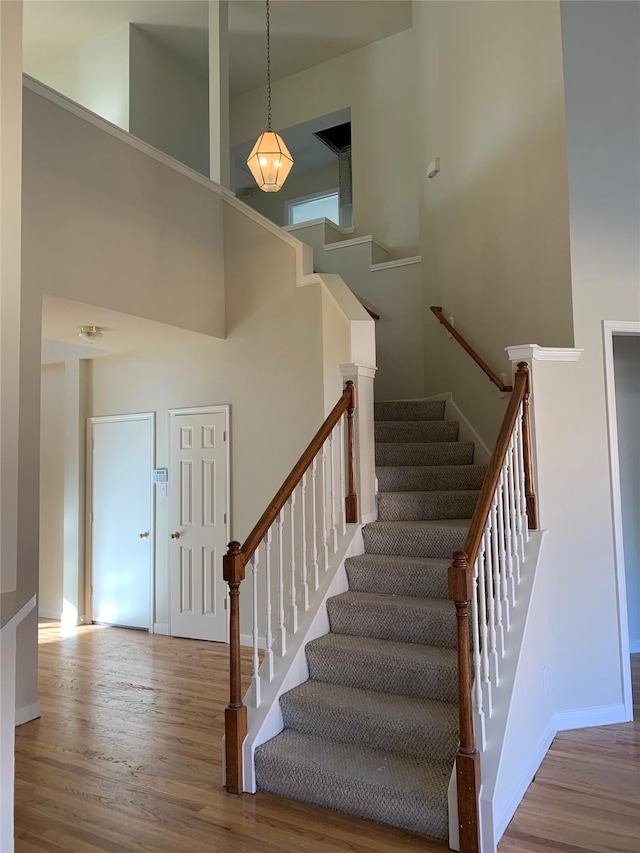 stairway featuring baseboards, wood finished floors, and a high ceiling