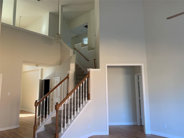 stairs with baseboards, wood finished floors, a high ceiling, and ceiling fan