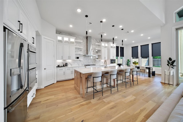 kitchen featuring open shelves, light wood-style floors, wall chimney exhaust hood, white cabinets, and stainless steel appliances